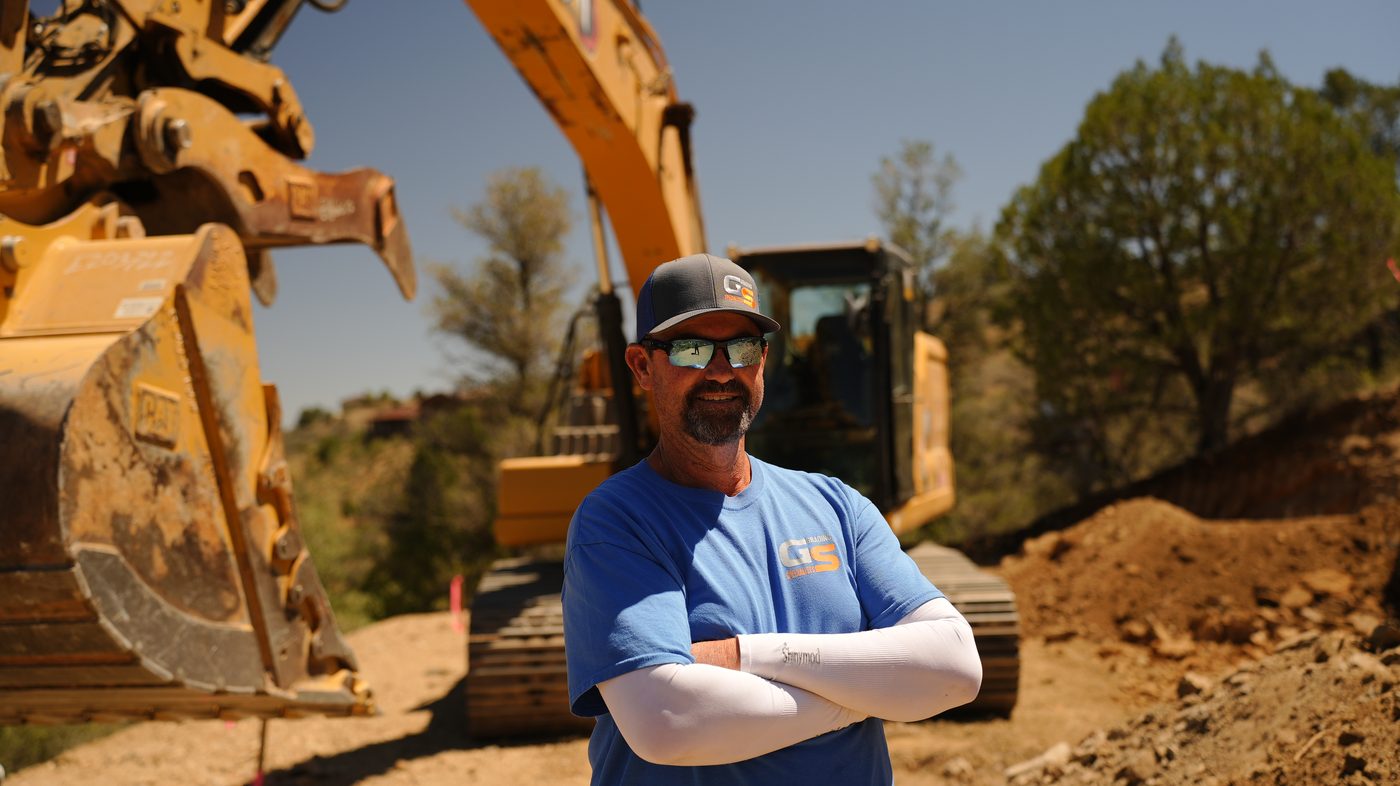 Owner of Grading Specialists standing in front of a CAT excavator on a Yavapai County job site